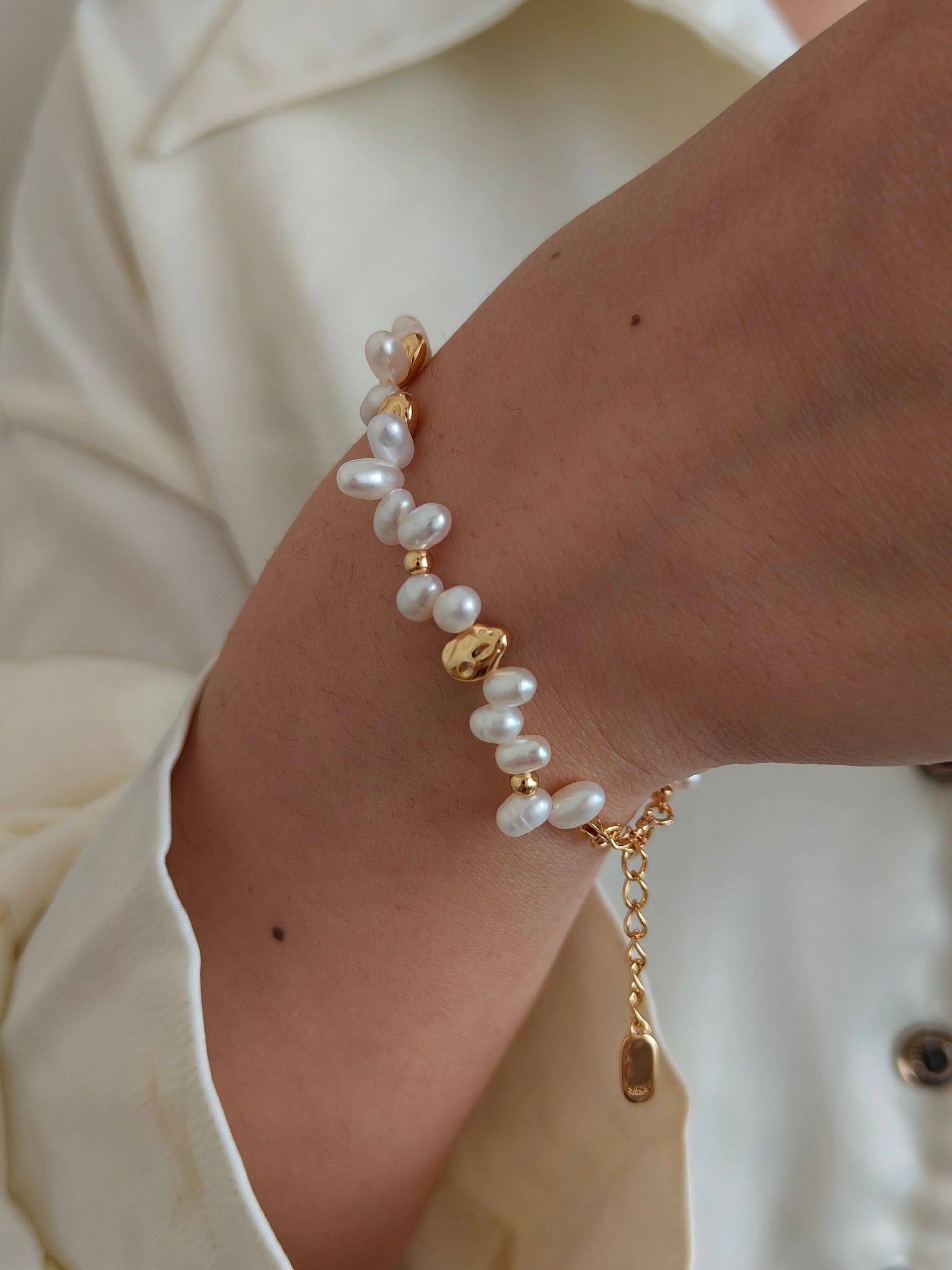 Freshwater pearl bracelet on wrist with gold bead spacers and small charm