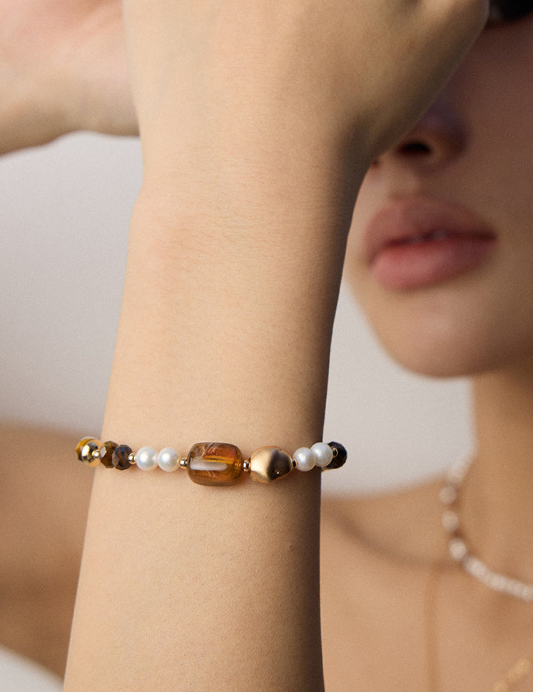 Bracelet on wrist with white pearls, black beads, brown tiger eye stones, and gold clasp