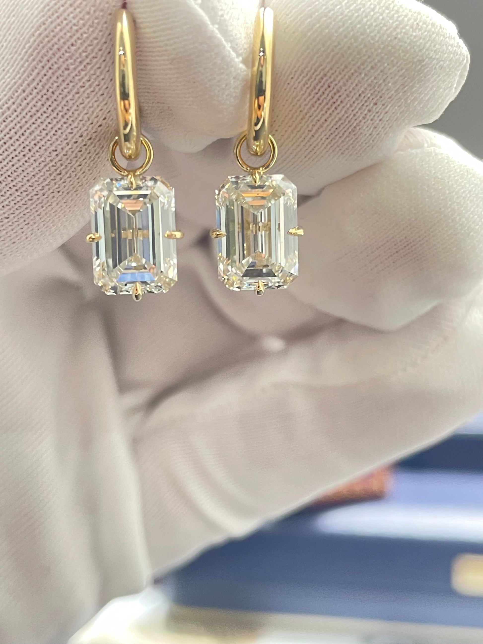 Gold hoop lab diamond earrings with emerald-cut stones, dangling.
