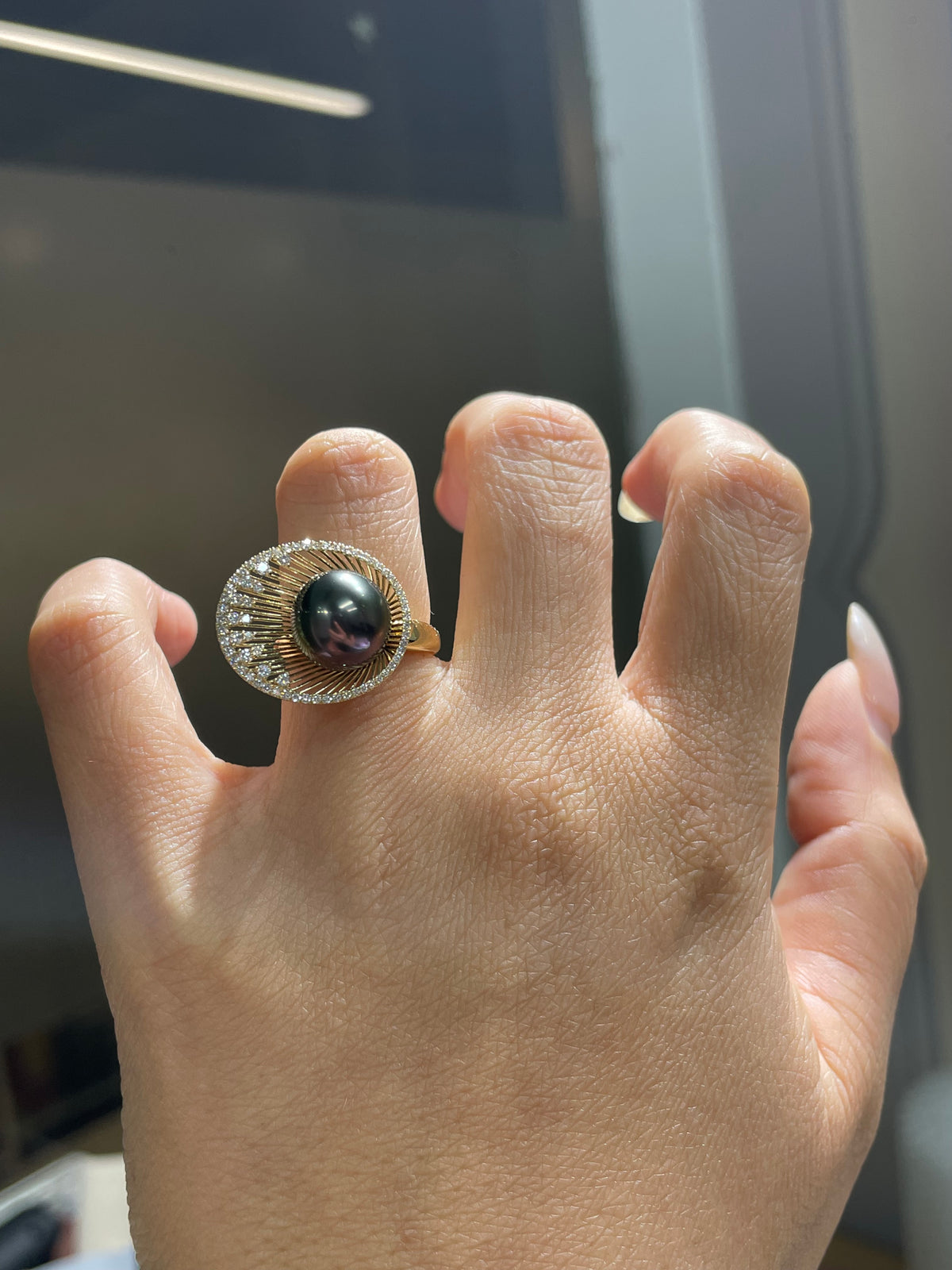 Yellow-gold ring with round dark Tahitian pearl and diamond halo, open prong detail